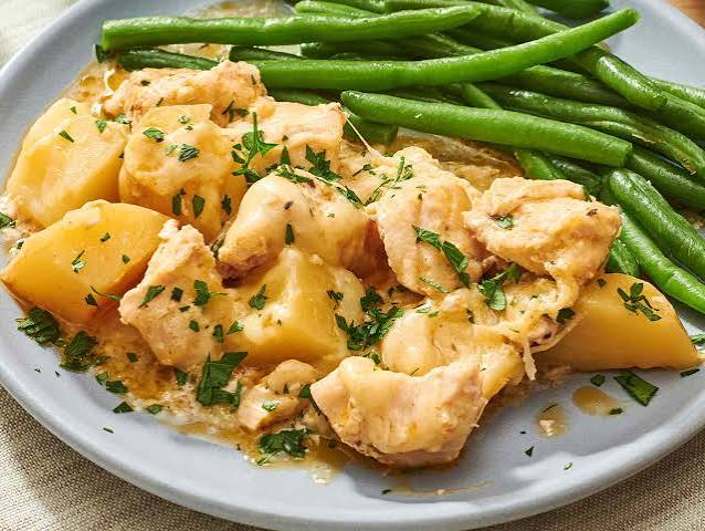 Bir tabak tavuk, patates ve yeşil fasulye yemeği, üzeri taze otlarla süslenmiş.
