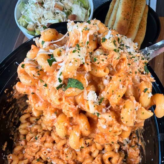 Büyük bir kapta, kremalı sosla karıştırılmış makarna; yanında yeşil salata ve ekmek dilimleri.